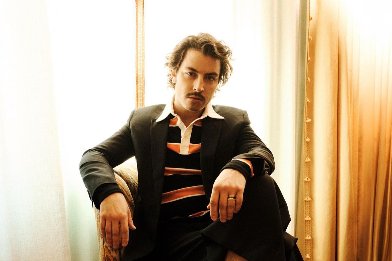 Boran Kuzum sits in a patterned armchair wearing a tailored suit during the GQ Middle East shoot, New York, United States, April 29, 2026. (Courtesy of BKM)