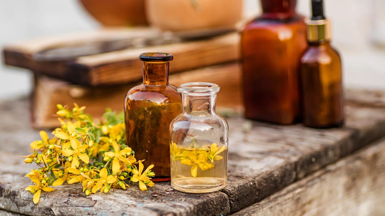 Infused herbal oil and fresh St. John’s Wort are displayed alongside traditional glass bottles used for storage. (Adobe Stock Photo)