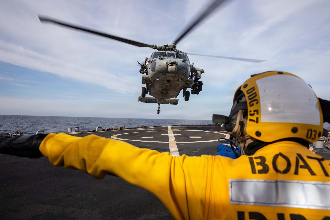A U.S. Sailor signals to an MH-60S Sea Hawk helicopter on the flight deck of the Arleigh Burke-class guided-missile destroyer USS Mitscher (DDG 57), April 15, 2026. (Photo via U.S. Navy)