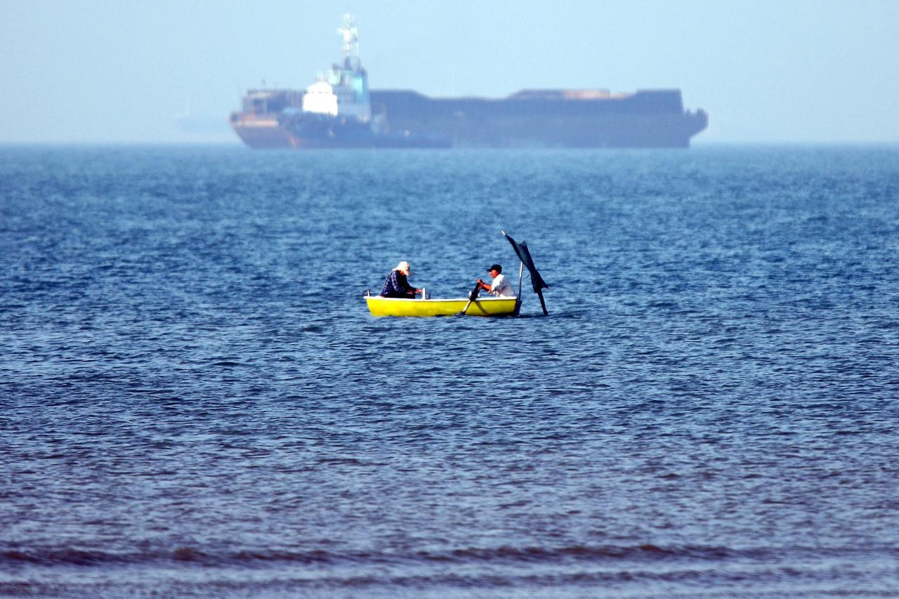In this picture obtained from Iran's ISNA news agency on May 4, 2026, two men sitting in a skiff are seen fishing near a vessel anchored in the Strait of Hormuz off Bandar Abbas in southern Iran. (AFP Photo)