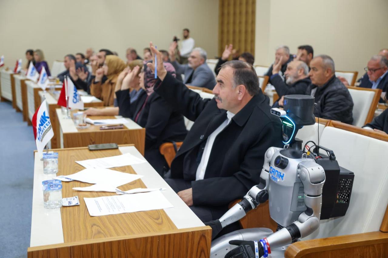 Council members raise their hands during a vote as CANIKMAN, Türkiye’s first population-registered humanoid robot, sits among participants at the Canik Municipal Council meeting in Samsun, Türkiye, May 5, 2026. (AA Photo)