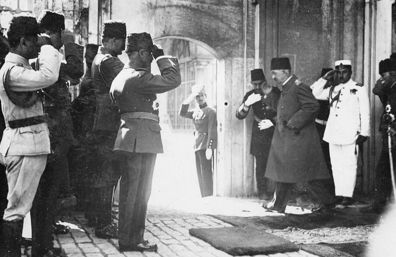 Sultan Mehmed VI Vahideddin departs from a rear entrance of Dolmabahce Palace in Istanbul as officials perform temenna, reflecting late Ottoman ceremonial etiquette. (Photo via Wikimedia)