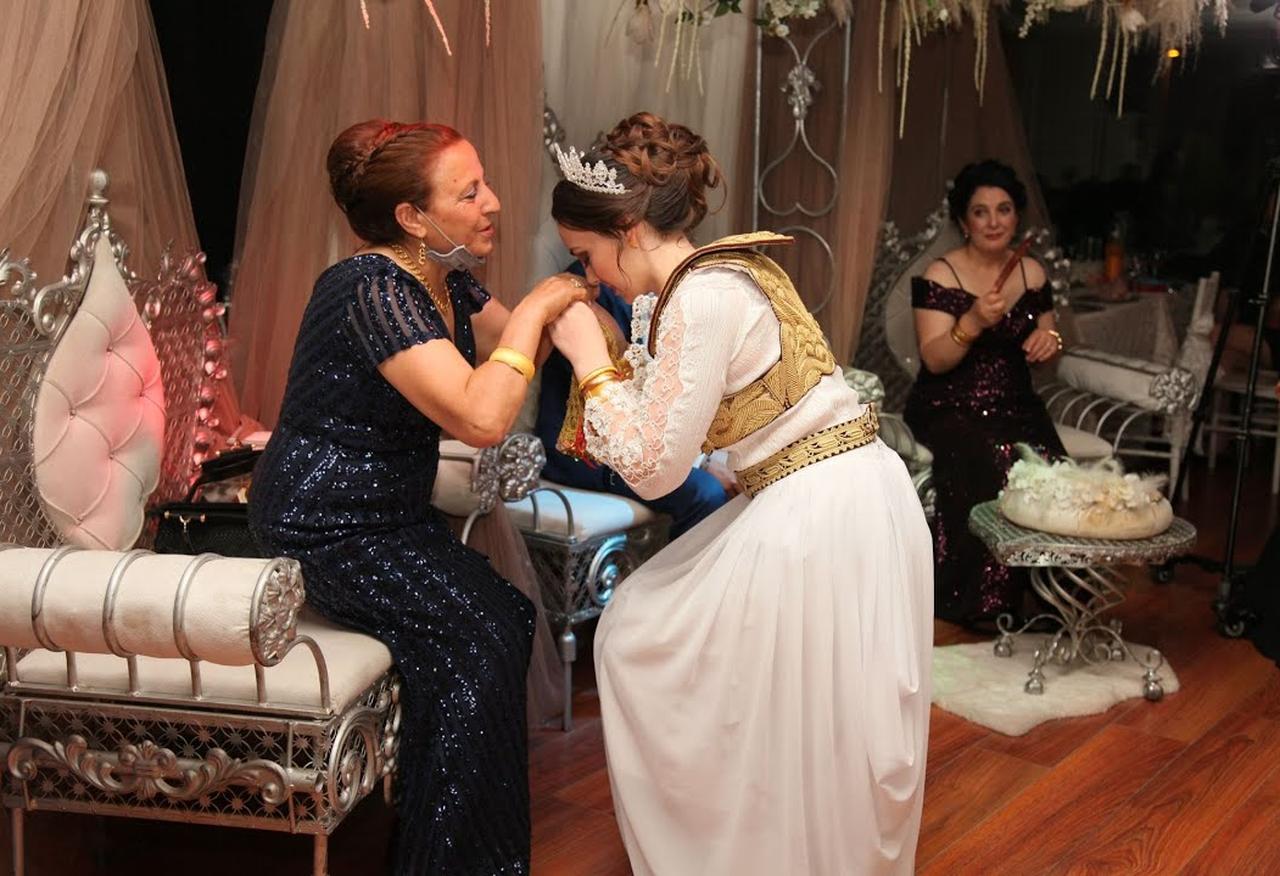 An Albanian bride performs a traditional gesture of respect by bowing and kissing her mother-in-law’s hand during a wedding ceremony, reflecting enduring customs of honor and family hierarchy. (Photo via YouTube/@busehalat8698)