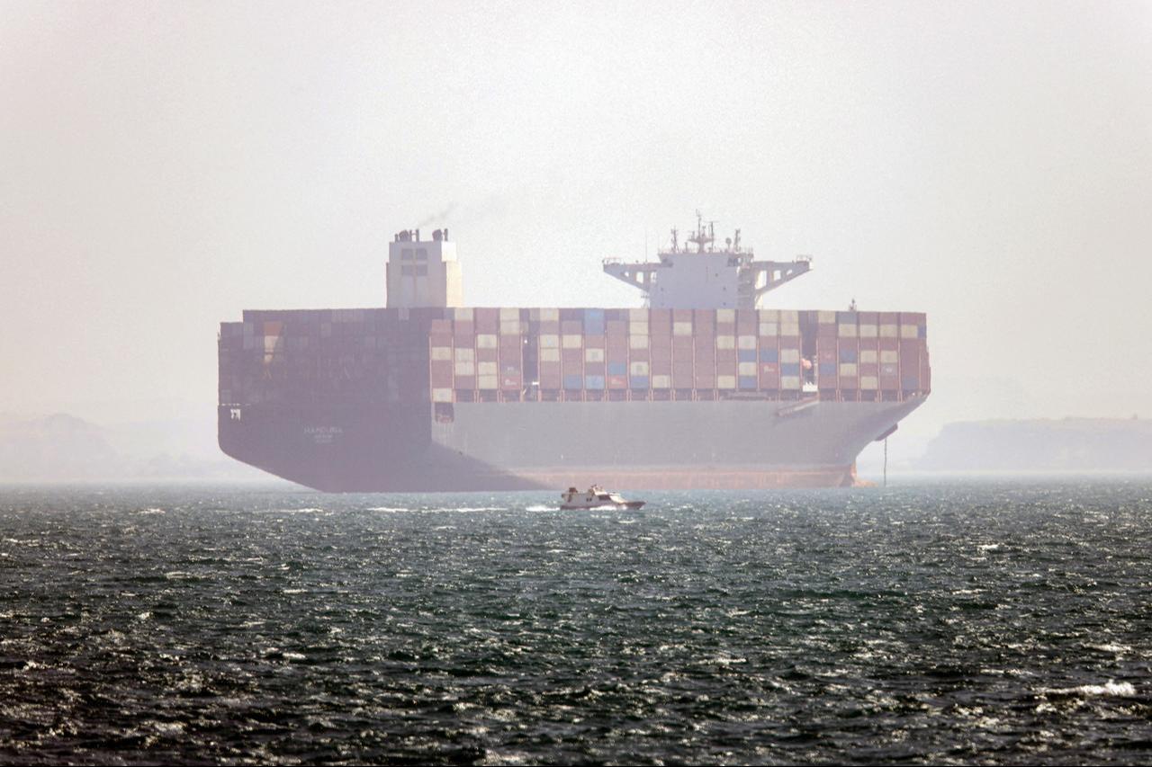 In this picture taken on May 2, 2026, the Iran-flagged container vessel Hamouna is pictured while anchored as a small motorboat passes by, in the Strait of Hormuz off Bandar Abbas in southern Iran. (AFP Photo)