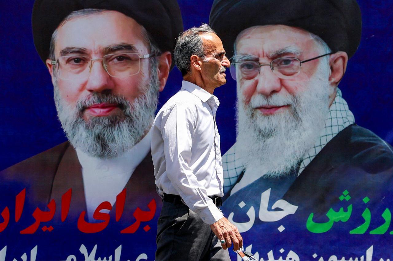 A man walks past a large banner depicting Iran's current supreme leader Ayatollah Mojtaba Khamenei and his predecessor and late father Ali Khamenei along a street in Tehran, May 6, 2026. (AFP Photo)