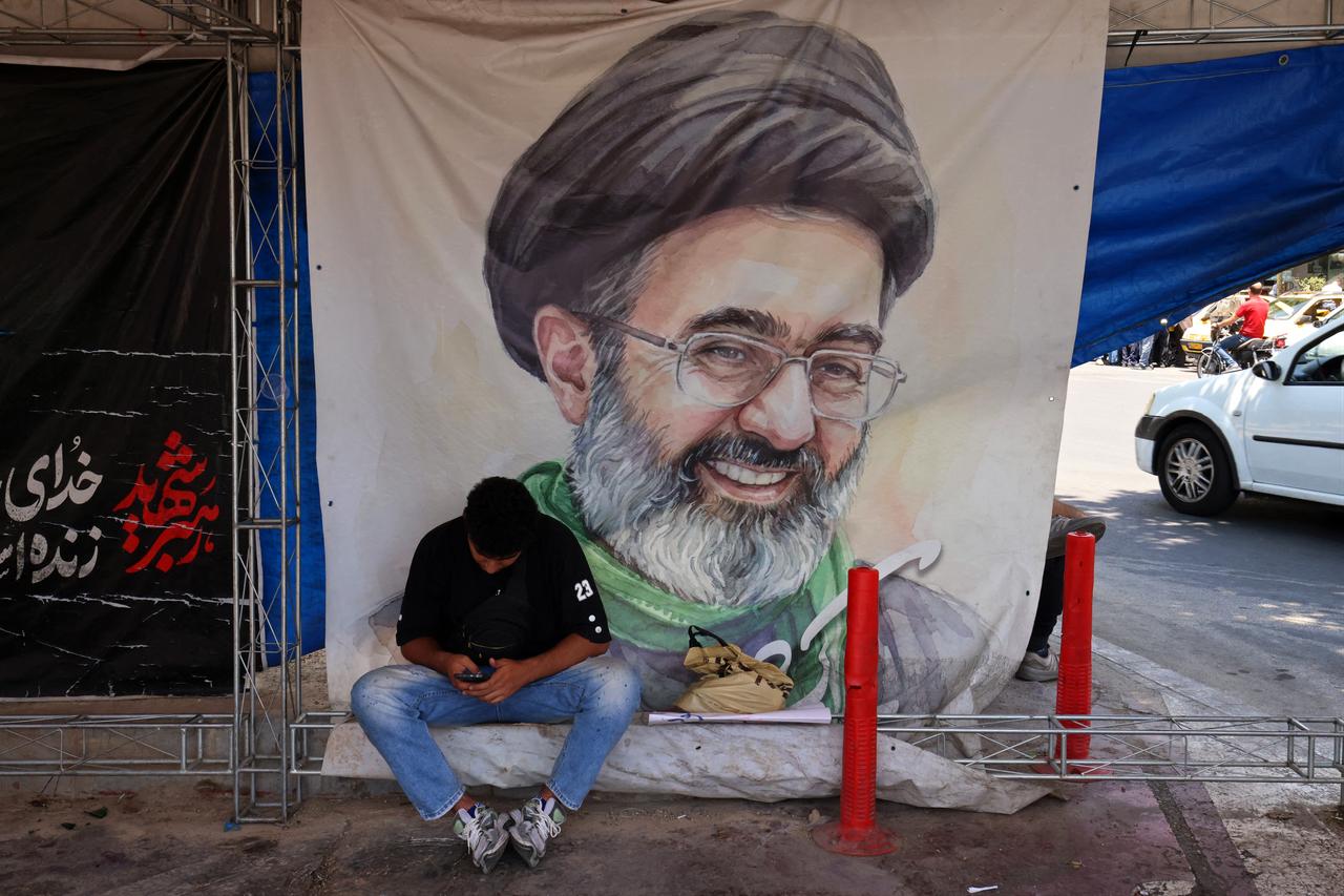 A man sits in front of a poster with portrait of Iranian supreme leader Mojtaba Khamenei, at the Vanak Square in Tehran, Iran, June 10, 2026. (AFP Photo)