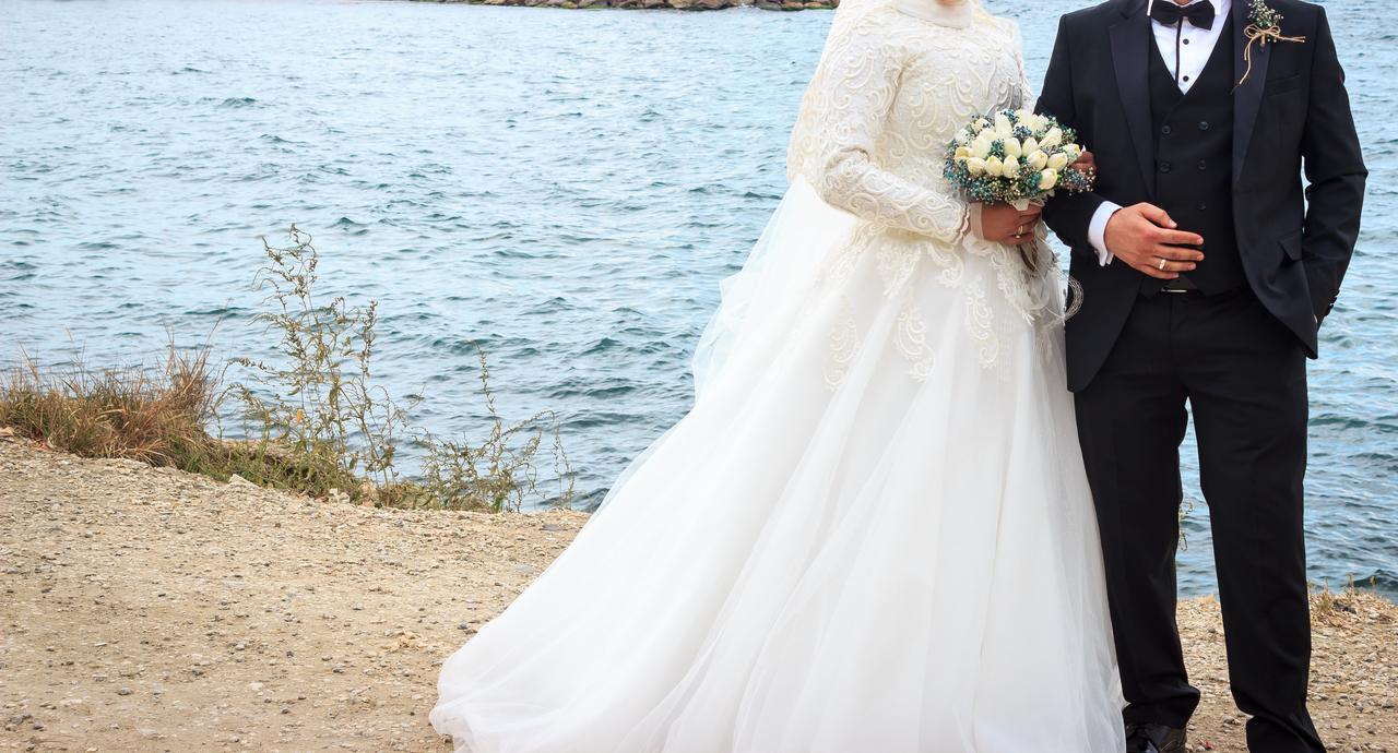 A newlywed couple poses by the waterfront during an outdoor wedding photo shoot, Türkiye. (Adobe Stock Photo)