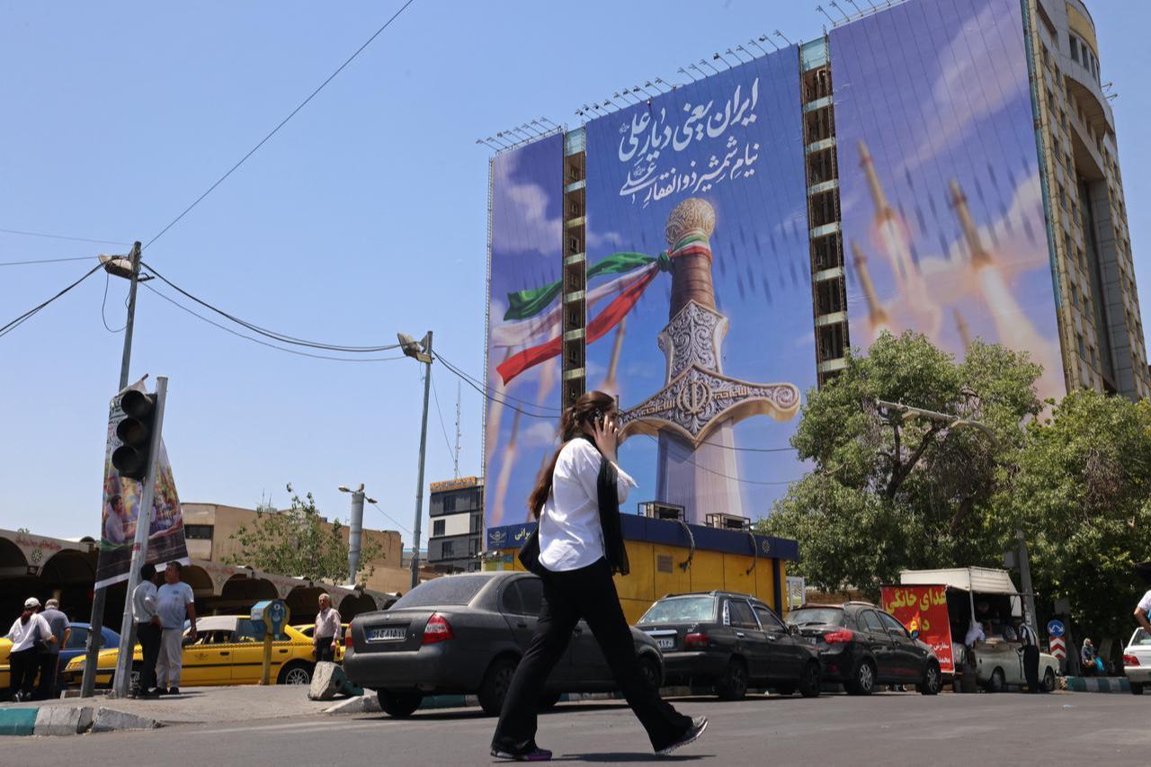 A woman walks past a giant banner depicting Iranian missiles and a sword belonging to Imam Ali, the first Imam of the Shiites, at Vanak Square in Tehran on June 10, 2026. (AFP Photo)