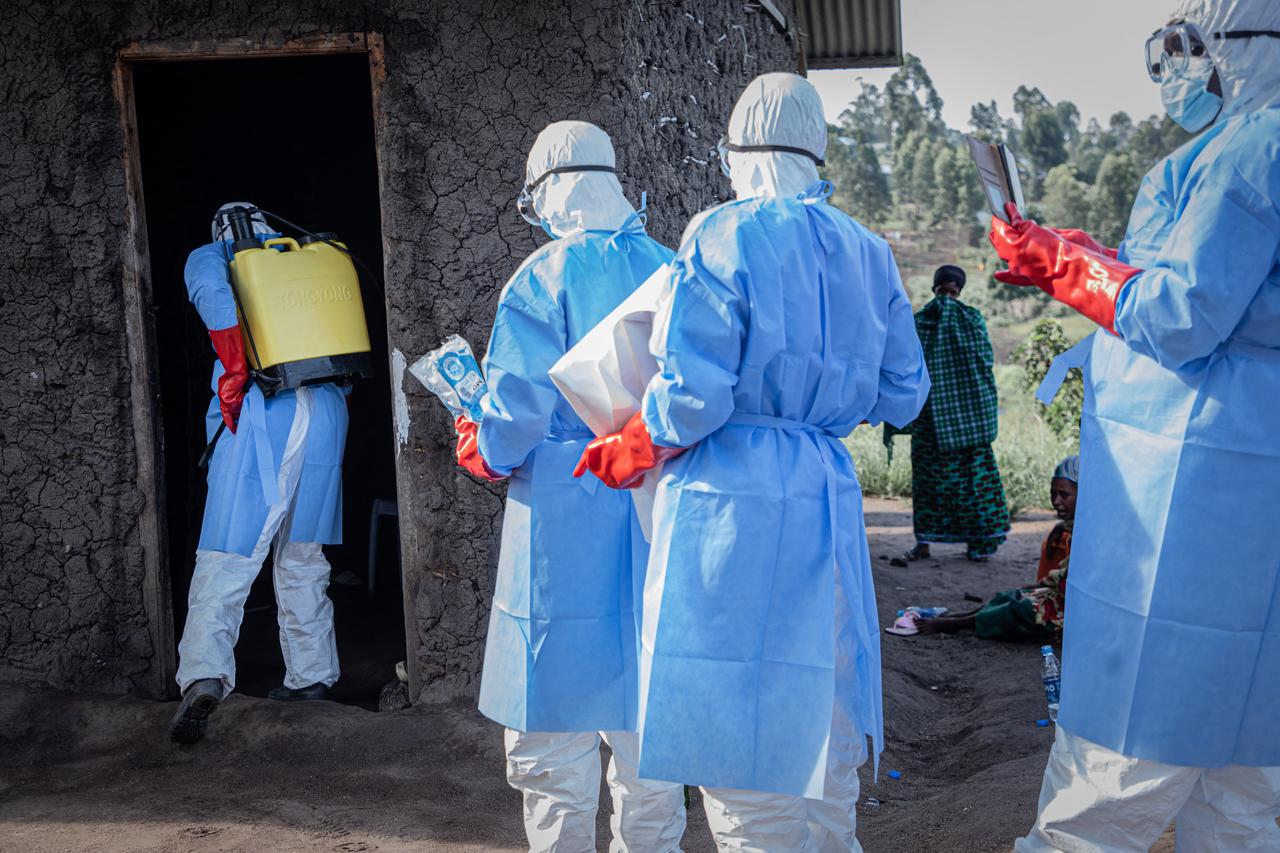 Un volontaire, portant un costume de protection, désinfecte la porte de la maison où se trouve un enfant, présumé mort de la maladie à virus Ebola, à Bunia, le 11 juin 2026. (Photo AFP)