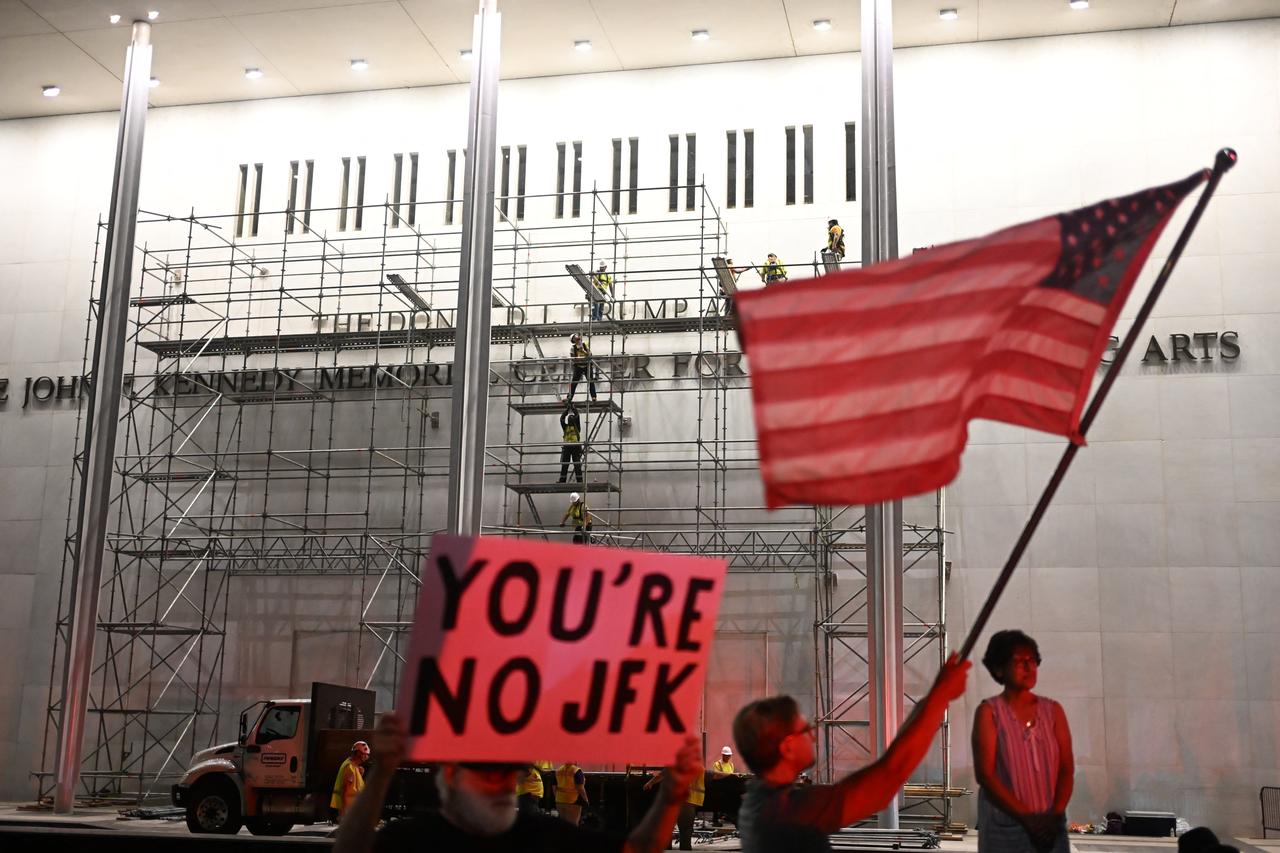 Protesters wave a US flag and hold a sign reading "you're no JFK" as workers build scaffolding near the signage for the "Donald J. Trump and John F. Kennedy Memorial Center for the Performing Arts" in Washington, DC, June 12, 2026. (AFP Photo)
