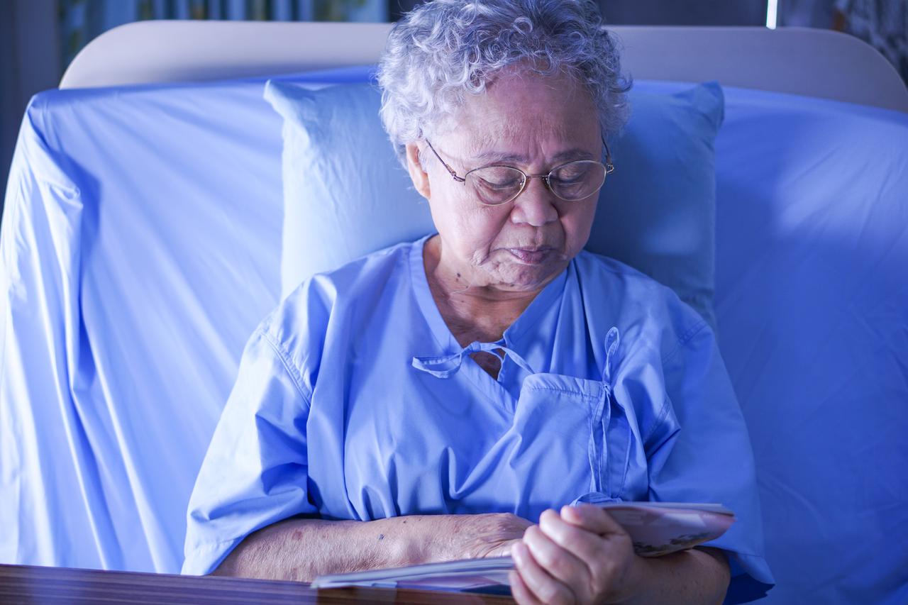 An older woman sits in a hospital bed holding a photobook. (Adobe Stock Photo)