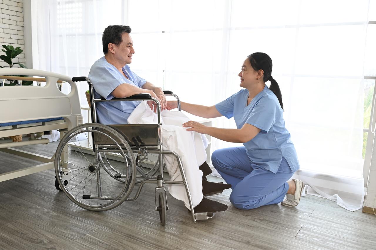 A caregiver assists an older man in a wheelchair (Adobe Stock Photo)