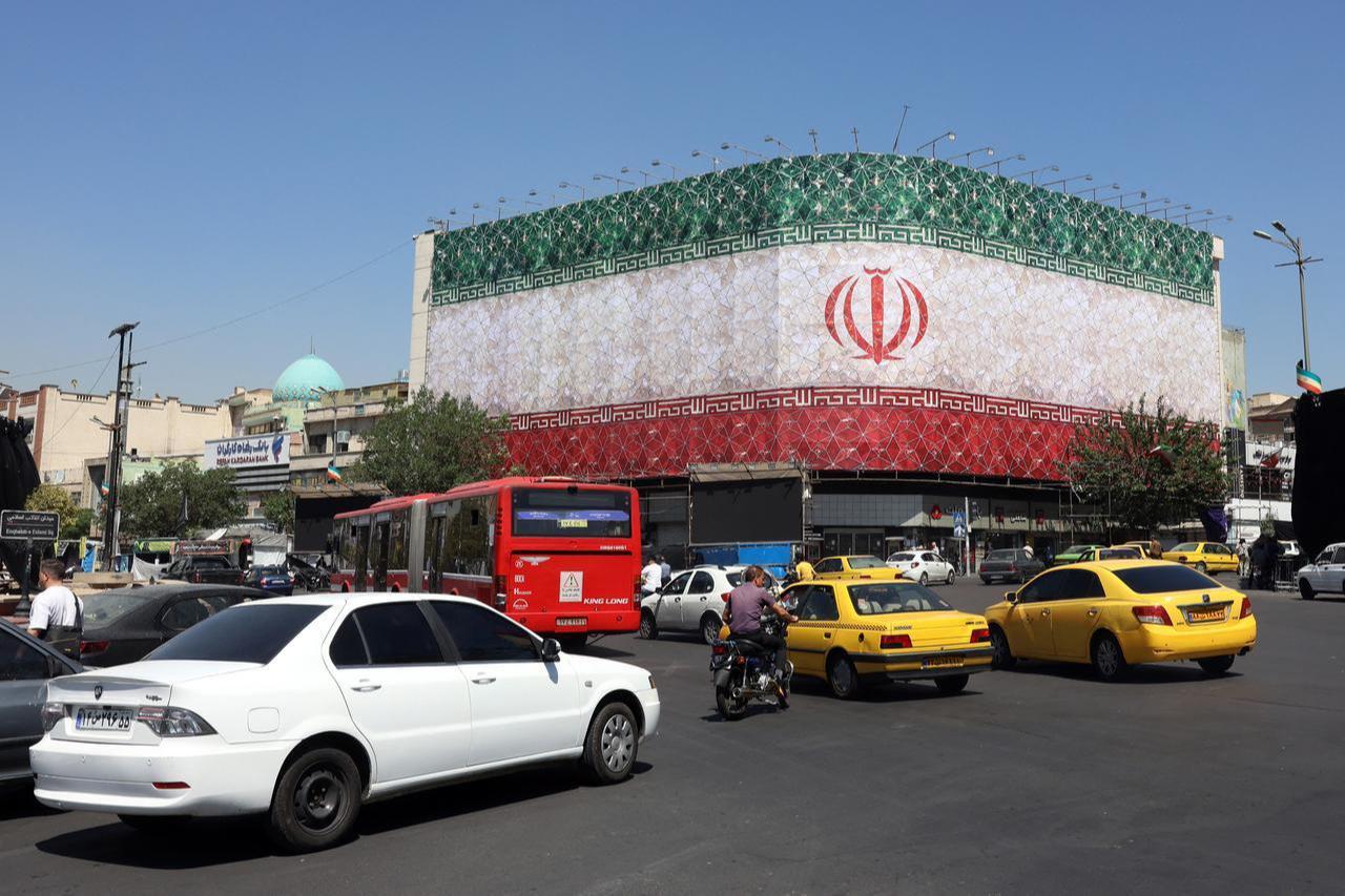 Traffic moves past the Iranian national flag displayed on a building at Enghelab Square in Tehran on June 14, 2026. (AFP Photo)