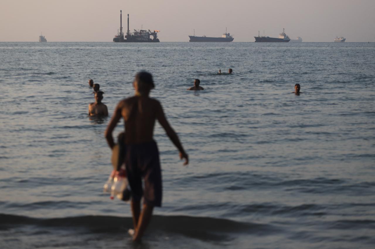 In this picture obtained from Iran's ISNA news agency on June 8, 2026, residents take a dip as cargo and commercial vessels lie at anchor in the Strait of Hormuz off Bandar Abbas. (AFP Photo)