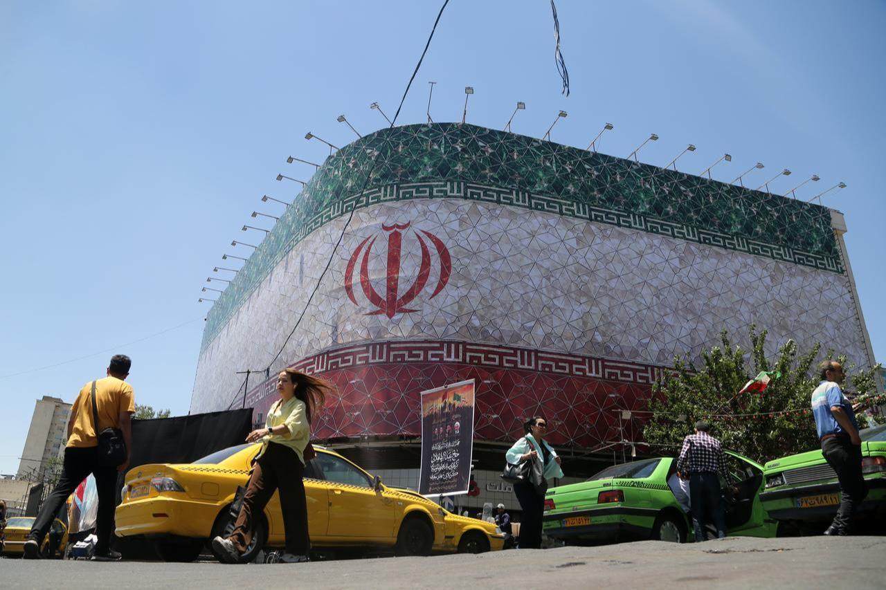 People walk past a billboard displaying Iran's national flag at Enghelab Square as daily life continues routinely in Tehran, Iran, June 15, 2026. (AA Photo)