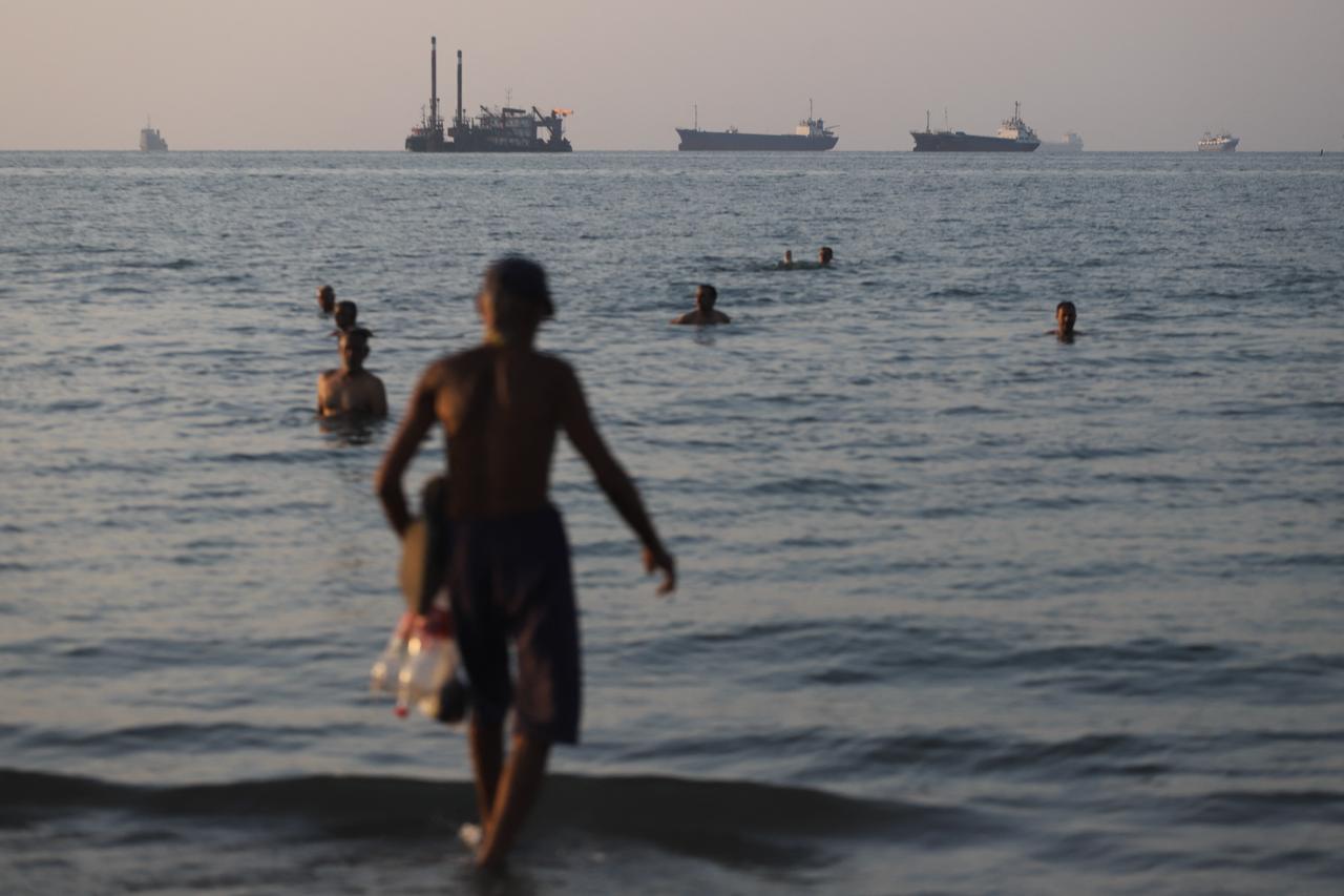 In this picture obtained from Iran's ISNA news agency on June 8, 2026, residents take a dip as cargo and commercial vessels lie at anchor in the Strait of Hormuz off Bandar Abbas. (ISNA/AFP Photo)