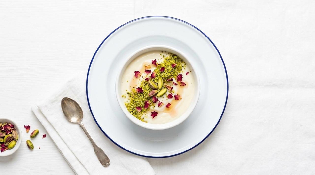 Muhallebi, served in a bowl, wearing a dusting of cinnamon, pistachio, and rose petals. (Adobe Stock Photo)
