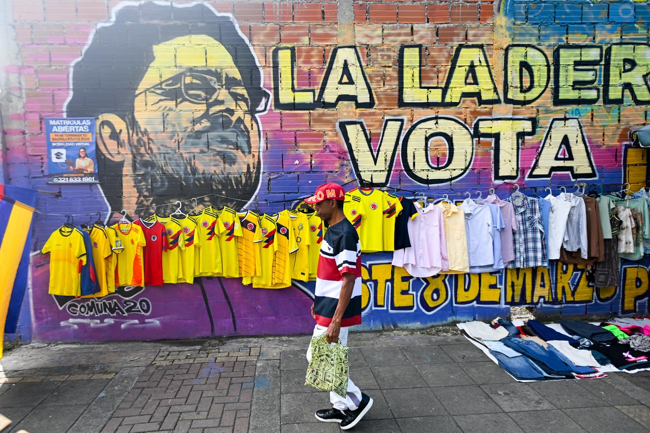 A man walks past Colombia's national football team jerseys for sale and a mural of presidential candidate Ivan Cepeda, of the Pacto Historico party, for the upcoming presidential election in Cali, Colombia, on June 18, 2026. (AFP Photo)
