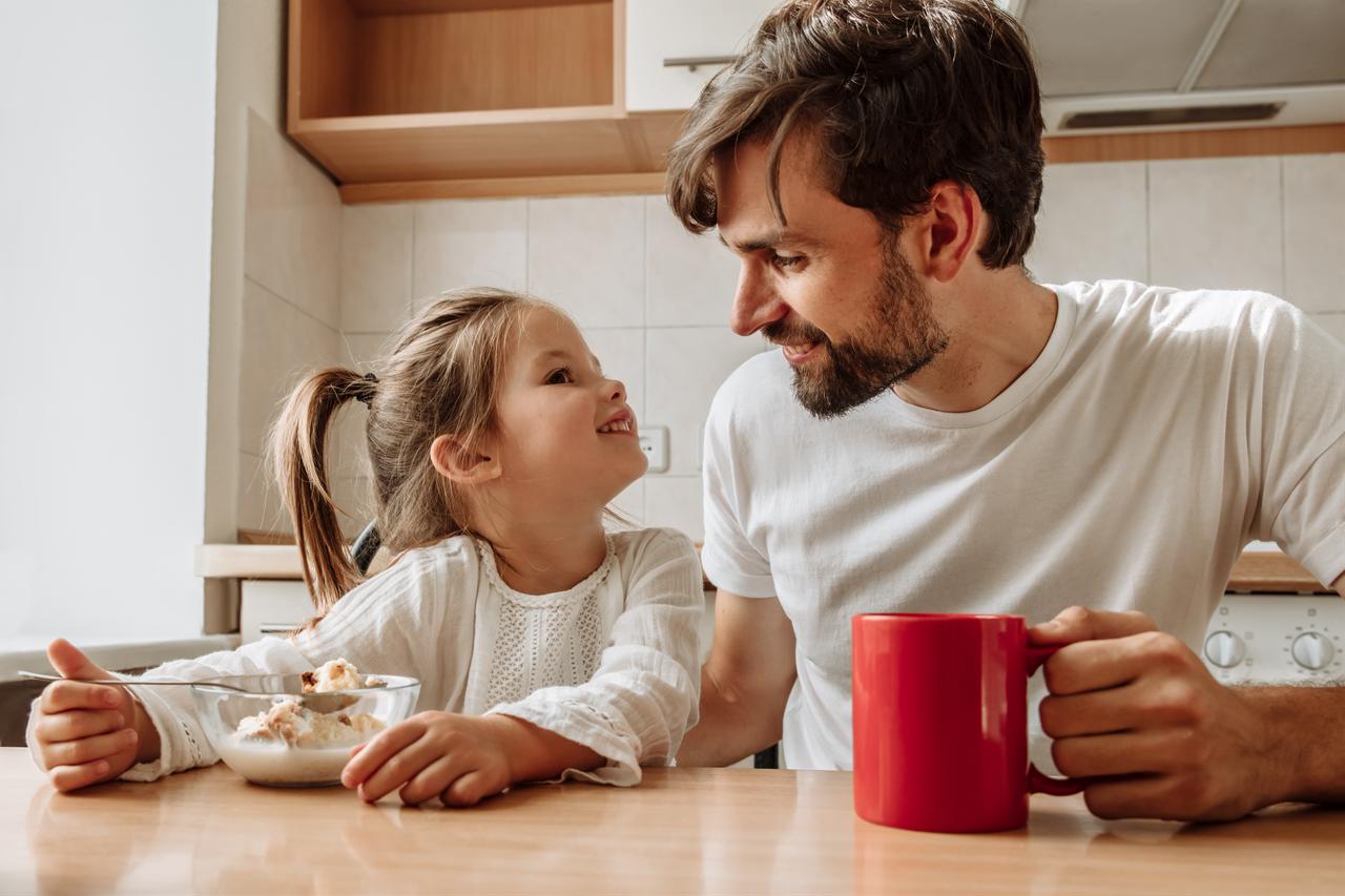 A father and daughter sit together at a kitchen table during breakfast (Adobe Stock Photo)
