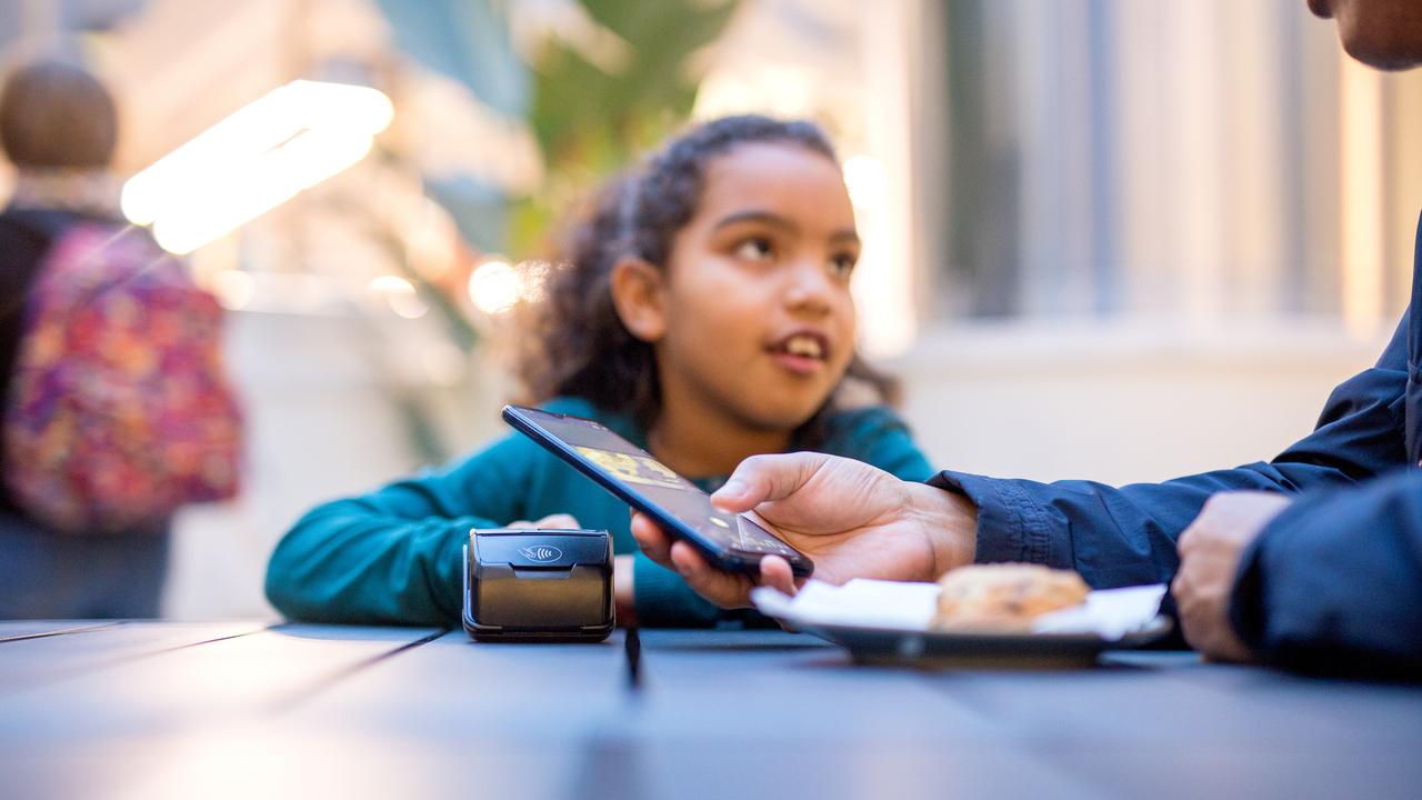 A person makes a contactless payment by phone as a child looks on at a cafe. (Adobe Stock Photo)