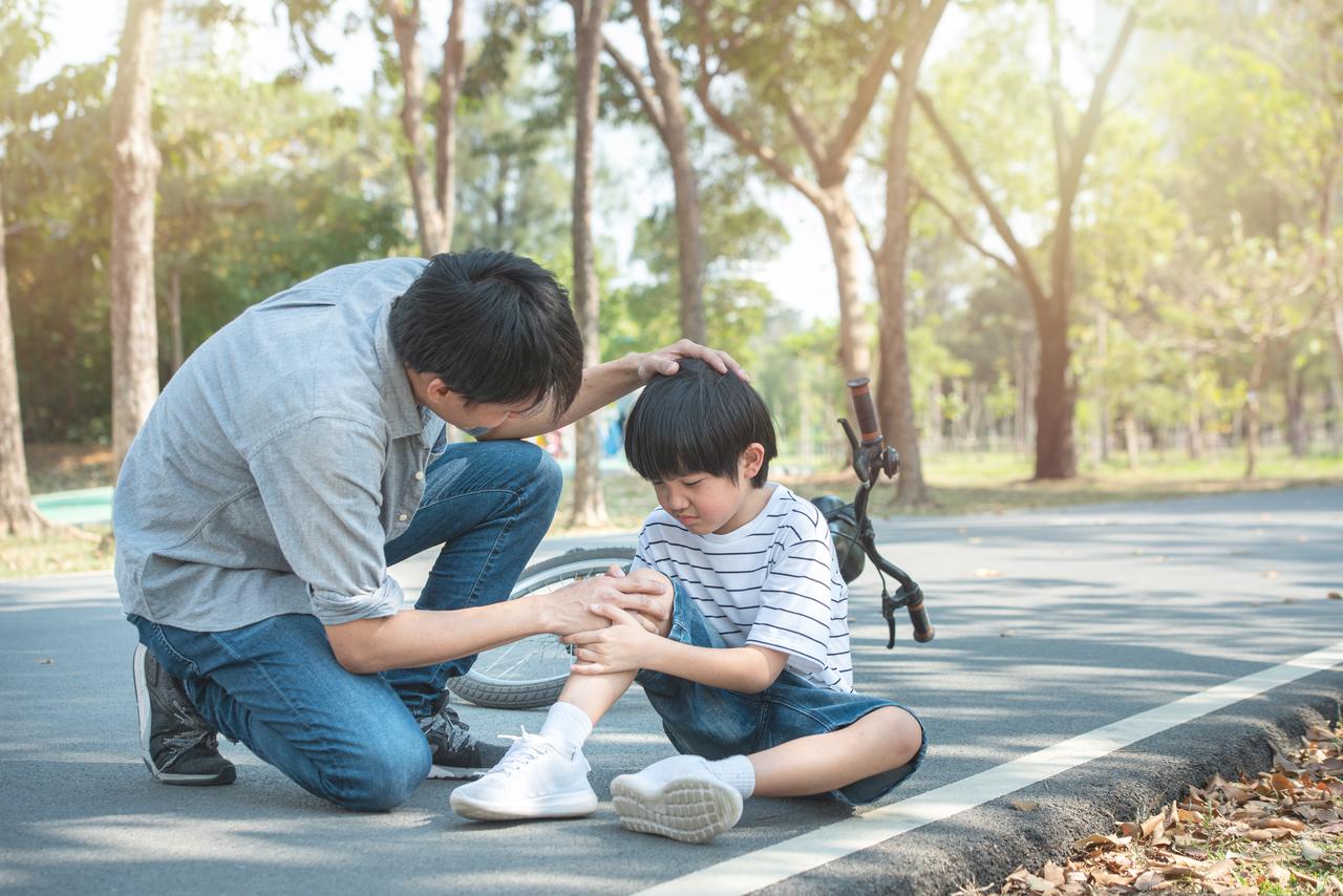 A father comforts his son after a bicycle fall. (Adobe Stock Photo)