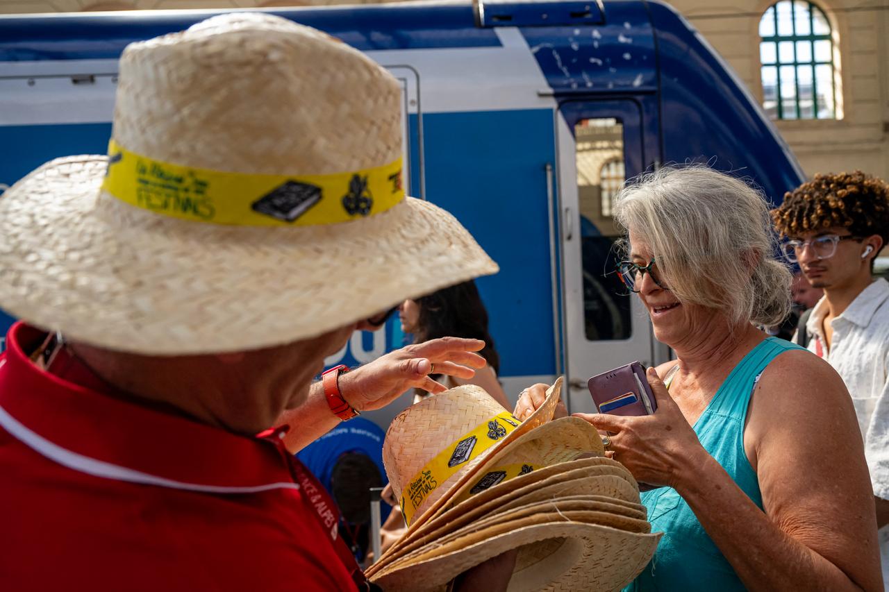 A staff member hands out hats to customers as part of a distribution of water bottles, hats and fans at the Saint-Charles railway station in Marseille, France, on June 22, 2026. (AFP Photo)
