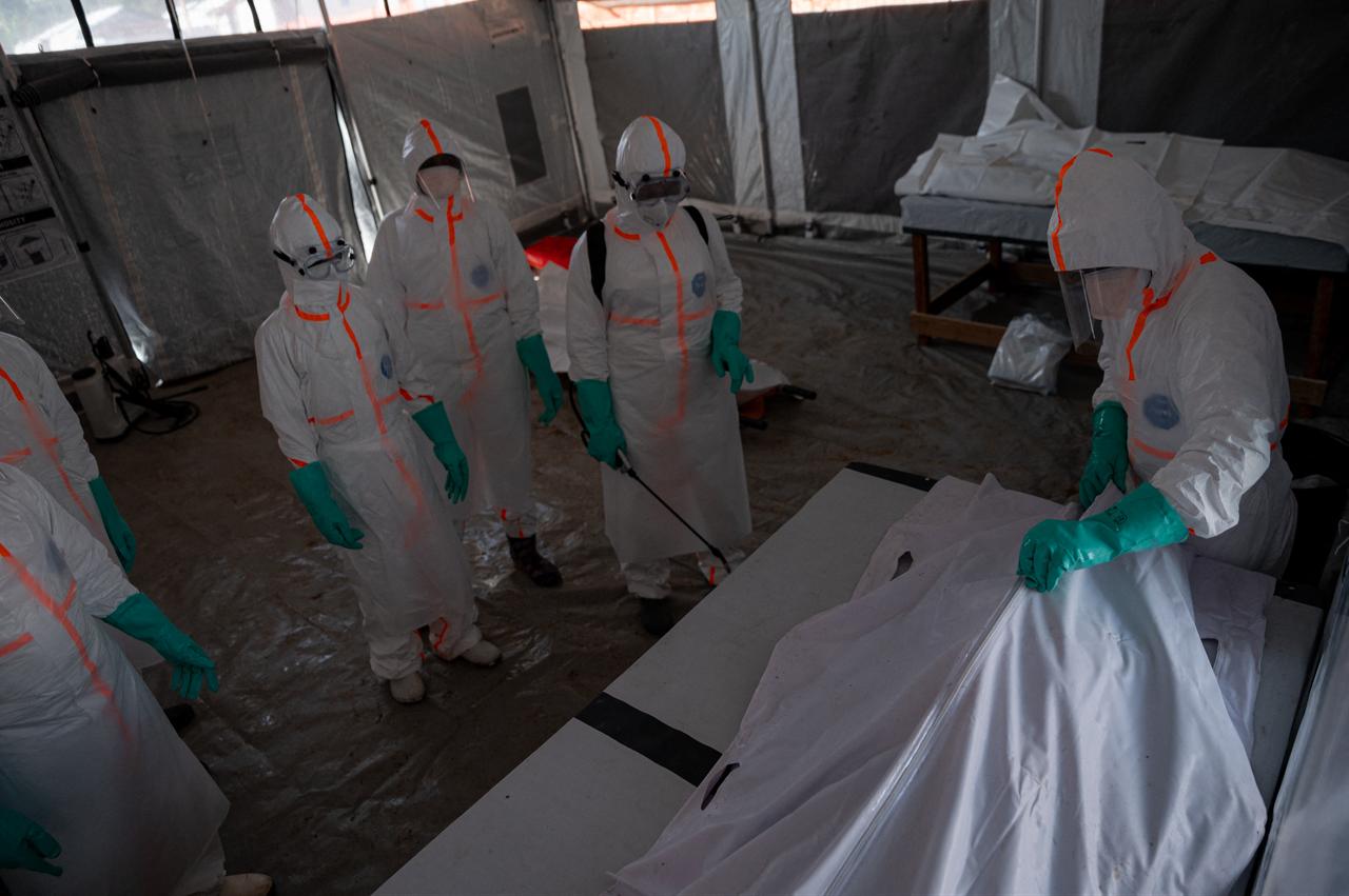 A team of doctors wearing protective suits works in a red zone inside the morgue, close a body bag containing the remains of a man who died from Ebola virus disease after having allowed the family see him for a last  moment before its transfer to the cemetery in Bunia, Ituri Province, Democratic Republic of the Congo, on June 13, 2026. (AFP Photo)