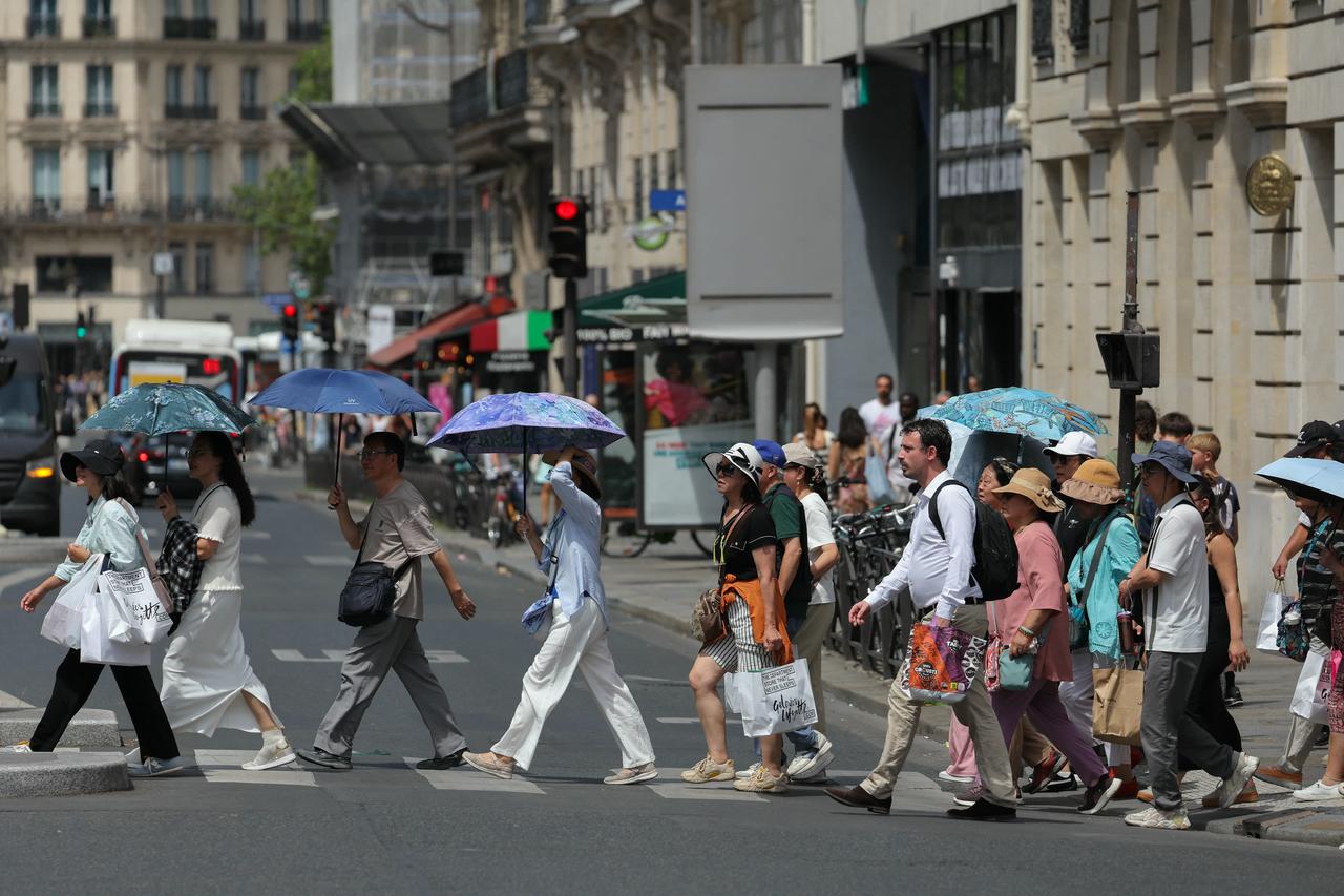 Tourists protect themselves from the sun under umbrellas while crossing a street in Paris, June 23, 2026. (AFP Photo)
