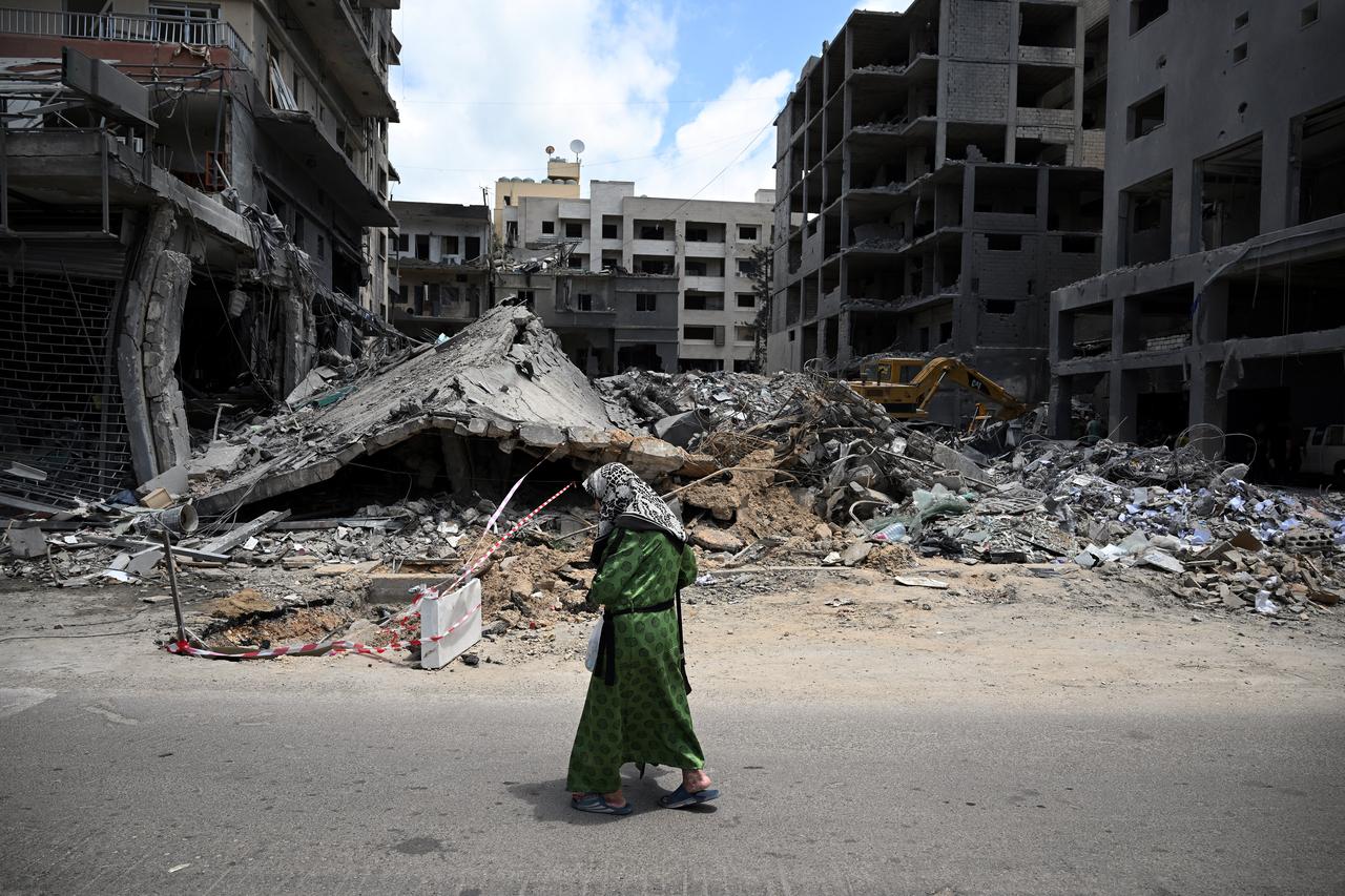 A woman walks past flattened building as workers remove the rubble from the site of an earlier Israeli military strike on a neighbourhood in the southern Lebanese coastal city of Tyre on June 23, 2026. On June 22, 2026, mediators Pakistan and Qatar said that Tehran and Washington had agreed to set up a "de-confliction cell" to limit flare-ups in Lebanon following talks in Switzerland on ending the wider Middle East war, which Tehran has linked to halting the parallel conflict in Lebanon. (Photo by Joseph EID / AFP) /