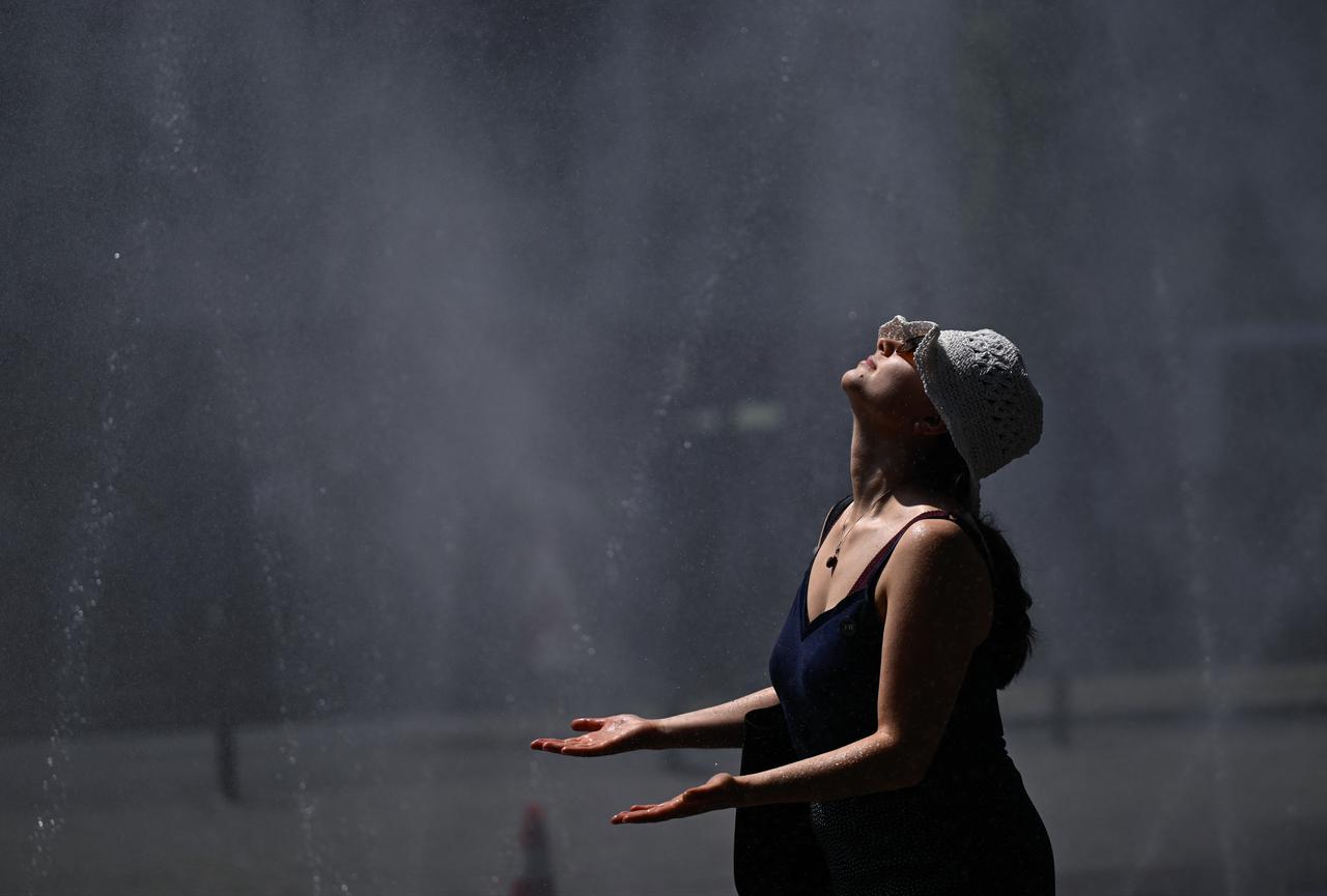 A woman cools down at water hoses spilling water to provide relief from the summer heat as part of Cologne’s climate adaptation measures in Cologne, western Germany on June 25, 2026. (AFP Photo)