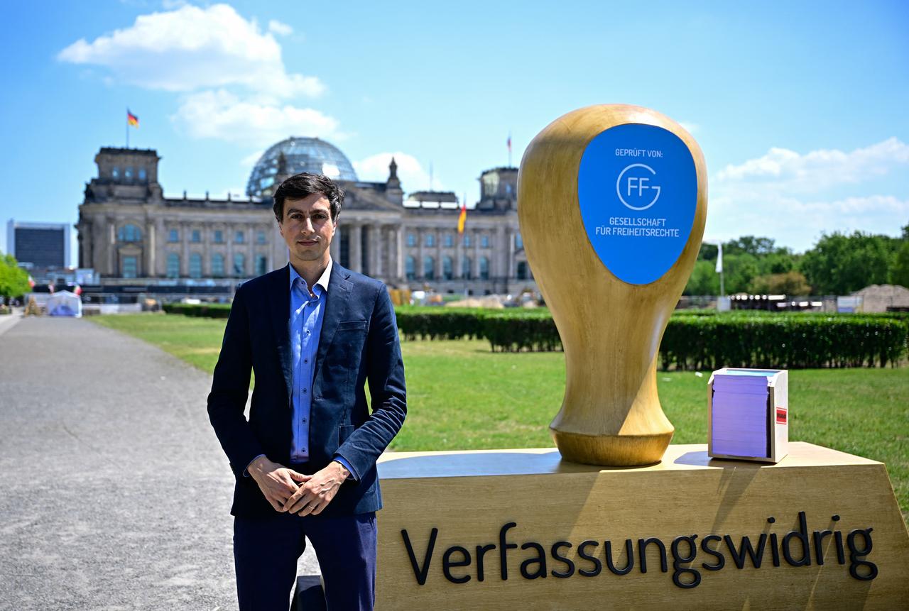 Bijan Moini, legal Director of the Society for Civil Rights (GFF) and project manager of a report on a possible unconstitutionality of the farright AfD party, poses next to the replica of an oversized stamp with the inscription "unconstitutional", on June 25, 2026 in front of the Reichstag building hosting the German parliament, the Bundestag in Berlin. (AFP Photo)