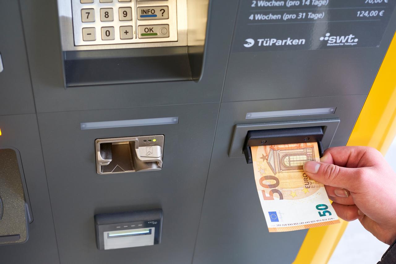 The photo shows a close-up of a person using a cash machine to insert a €50 bill, Tubingen, Germany, December 31, 2023. (Adobe Stock Photo)