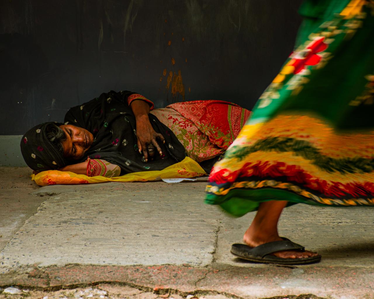 A woman lies on a sidewalk as another person walks past. (Adobe Stock Photo)