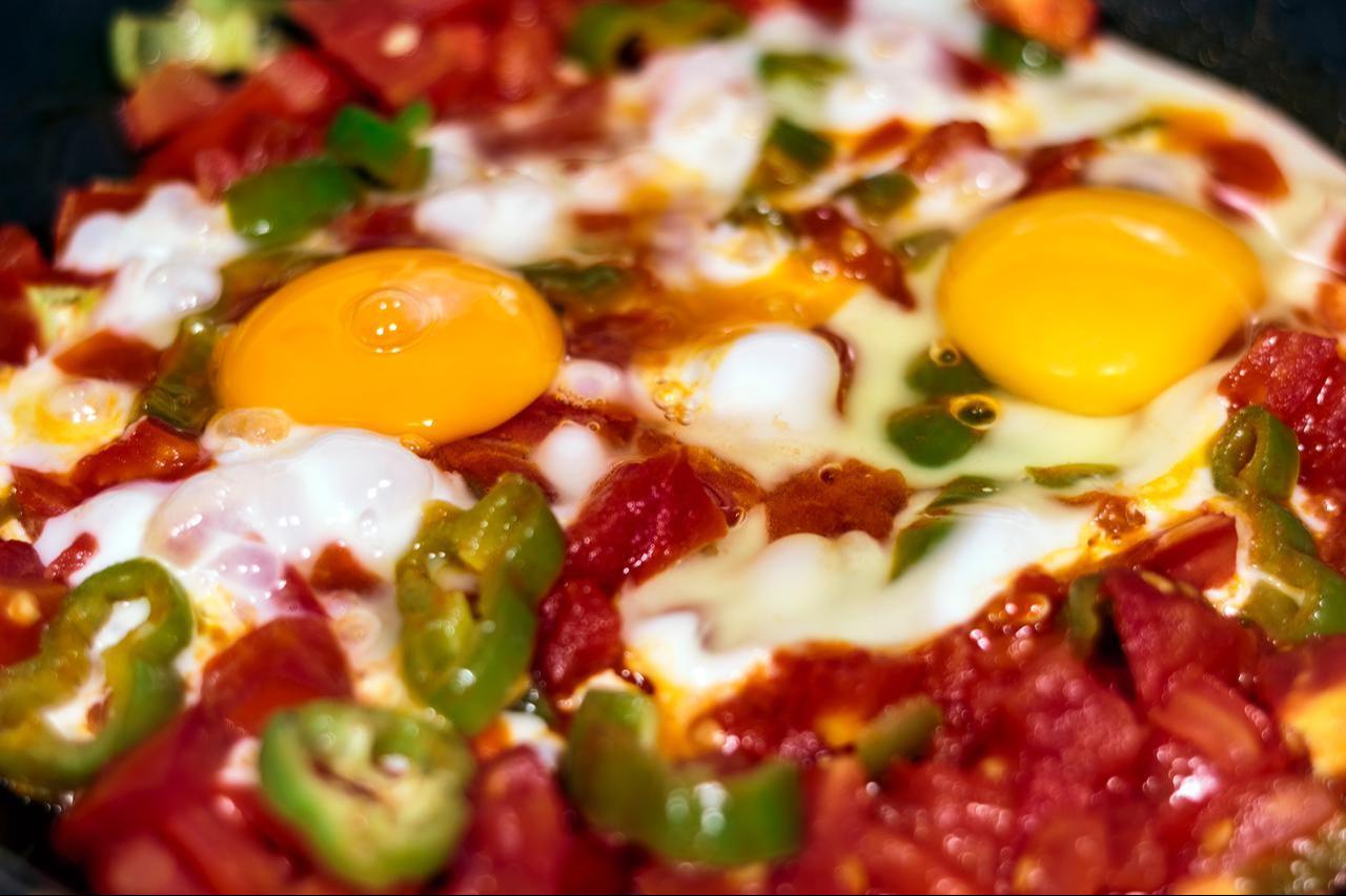 Eggs cook gently on top of a simmering mixture of chopped tomatoes and green peppers for a dish of menemen, accessed on June 3, 2026. (Adobe Stock Photo)