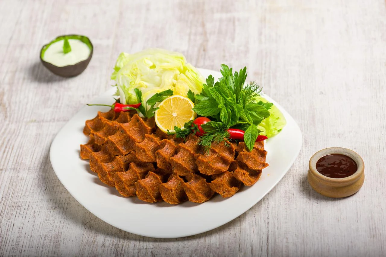 A plate of Turkish cig kofte shaped with distinctive ridges, garnished with fresh mint, parsley, lemon, and iceberg lettuce. (Adobe Stock Photo)