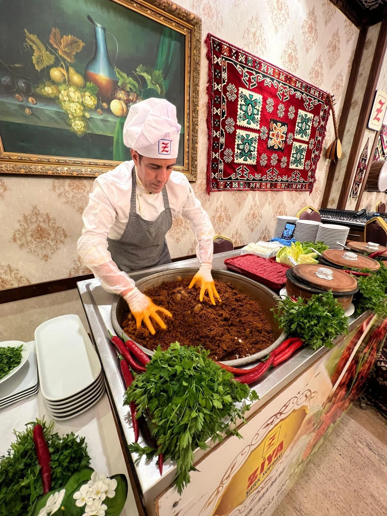 A master chef meticulously prepares a massive batch of traditional cig kofte, blending fine bulgur, fiery isot pepper, and fresh herbs through an intensive, time-honored process of continuous kneading. (Adobe Stock Photo)