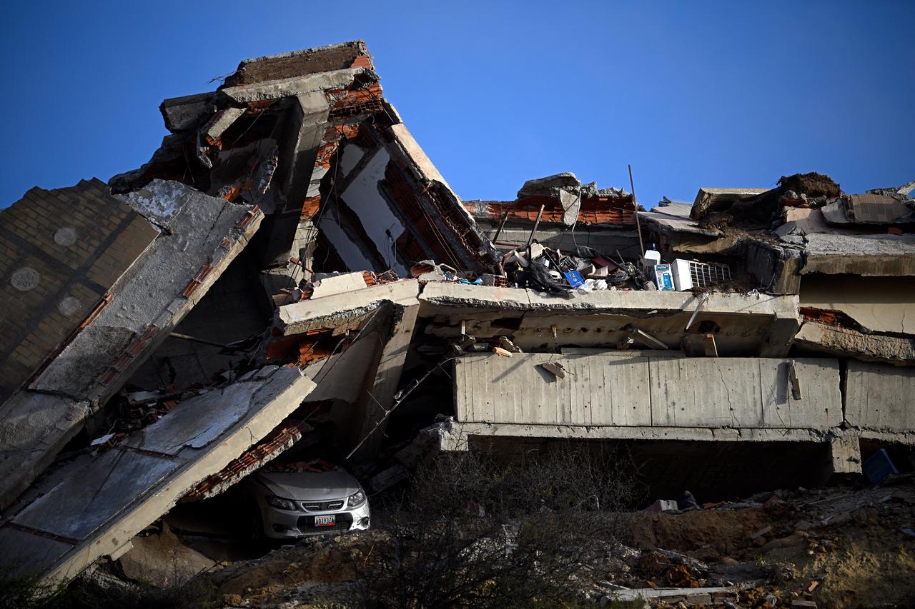 This view shows a collapsed concrete structure with crushed floors and debris, with a car partially buried beneath, in the Playa Verde sector of Catia La Mar, La Guaira state, Venezuela, on June 29, 2026, following twin earthquakes. (AFP Photo)