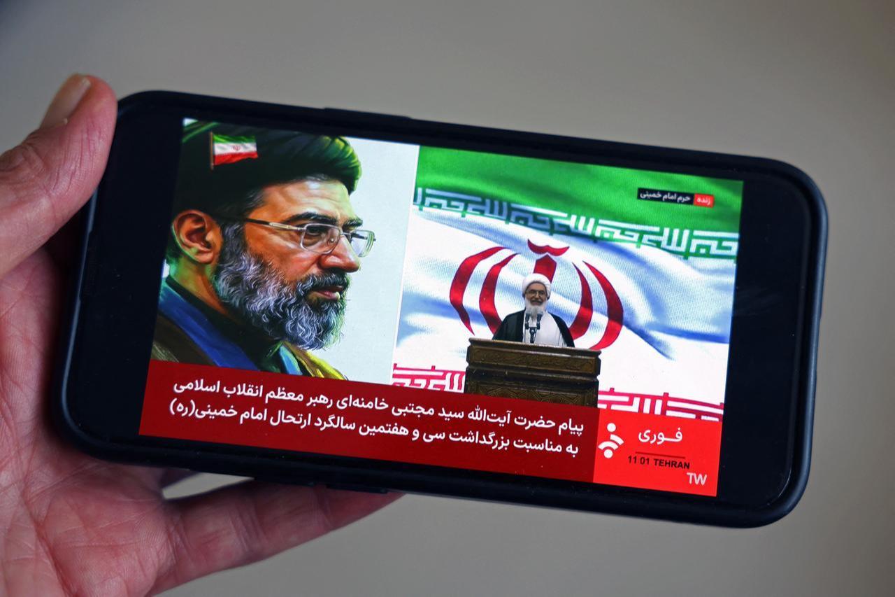 This illustration photograph taken on June 4, 2026, shows a man watching the live streaming on his mobile phone of an Iranian official reading a message by Iran’s supreme leader, Mojataba Khamenei, to the public at the tomb of the country's late supreme leader, Ruhollah Khomeini, in Tehran, June 4, 2026. (AFP Photo)