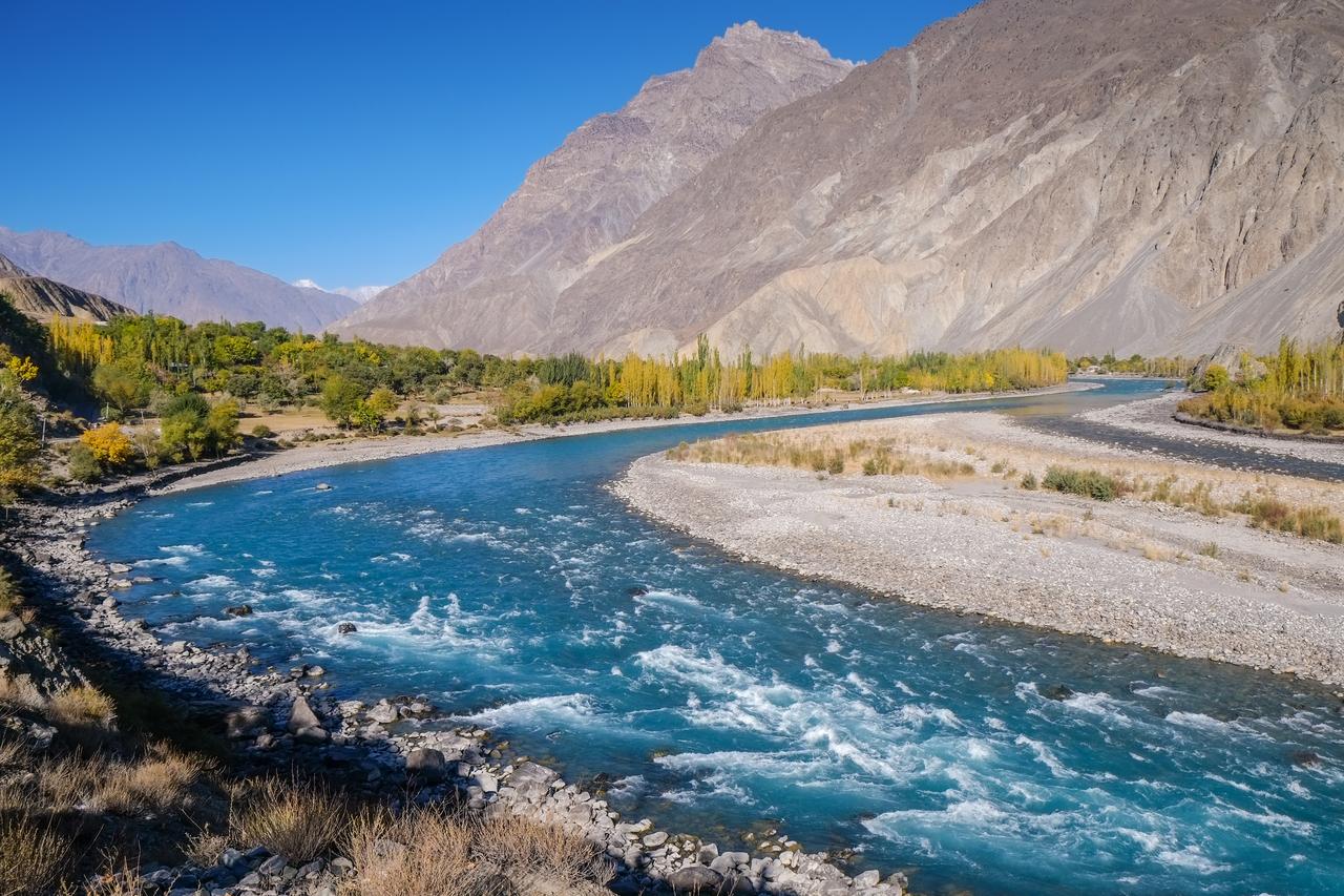Blue water of winding Gilgit river of Indus flowing through Gupis, Ghizer with mountains and autumn forest. Gilgit Baltistan, Pakistan. (Adobe Stock photo)