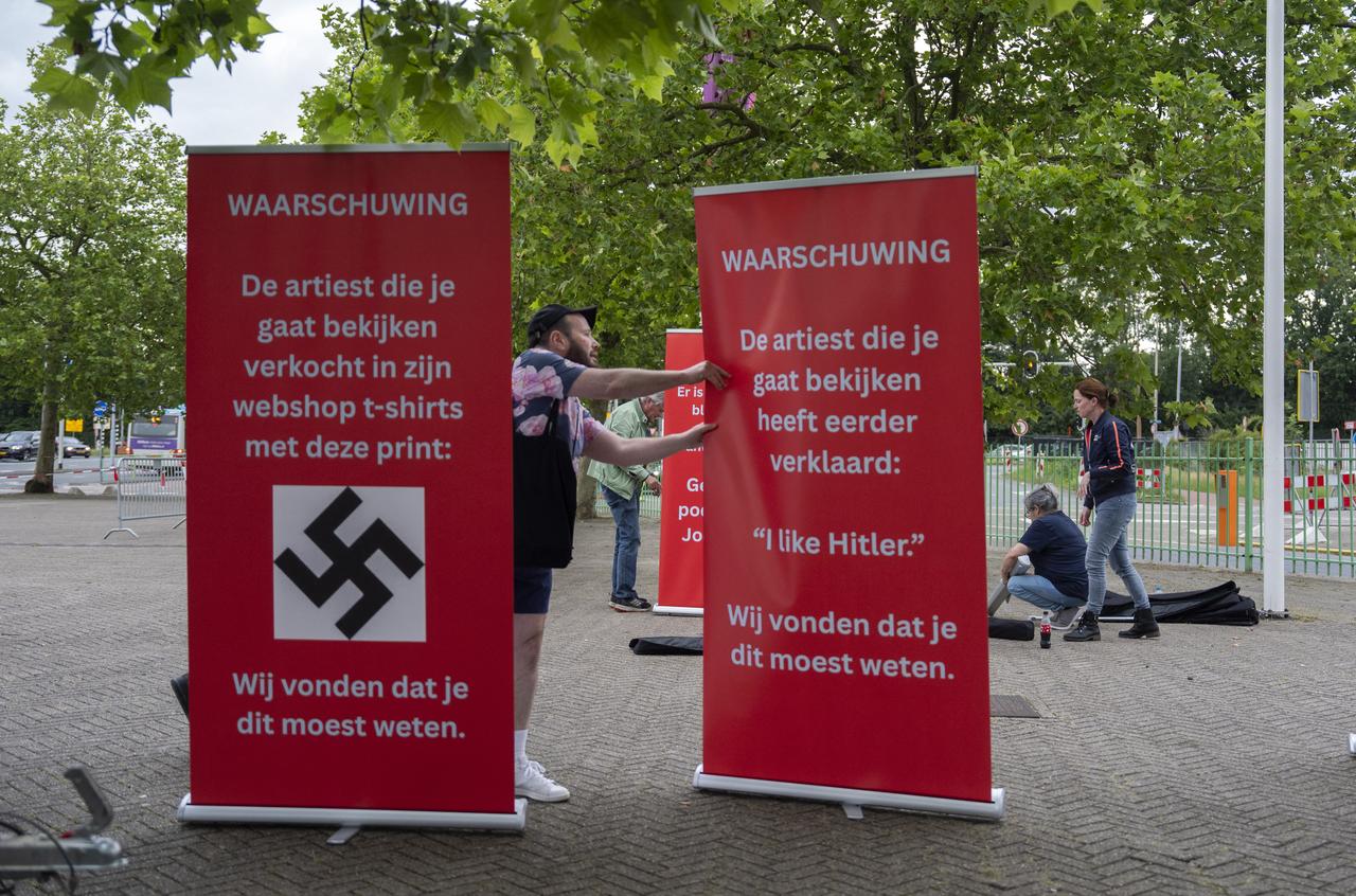 A demonstrator installs banners reading "WARNING - The artist you are about to see previously stated: 'I like Hitler' We thought you should know this." (R) and "WARNING - The artist you are about to see sold T-shirts with this print on their webshop - We thought you should know this." and depicting the image of a swastika during a protest outside the GelreDome venue, in Arnhem, Netherlands on June 6, 2026. (AFP Photo)