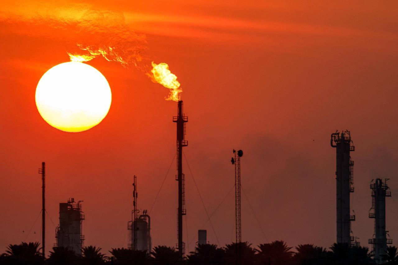 The sun sets behind the Dora (Daura) Oil Refinery Complex in Baghdad on December 22, 2024. Oil prices slumped on May 5, 2025 after eight OPEC+ members announced a sharp increase in production, while Asian stocks treaded water in thin trade with major markets closed. (Photo by AHMAD AL-RUBAYE / AFP)