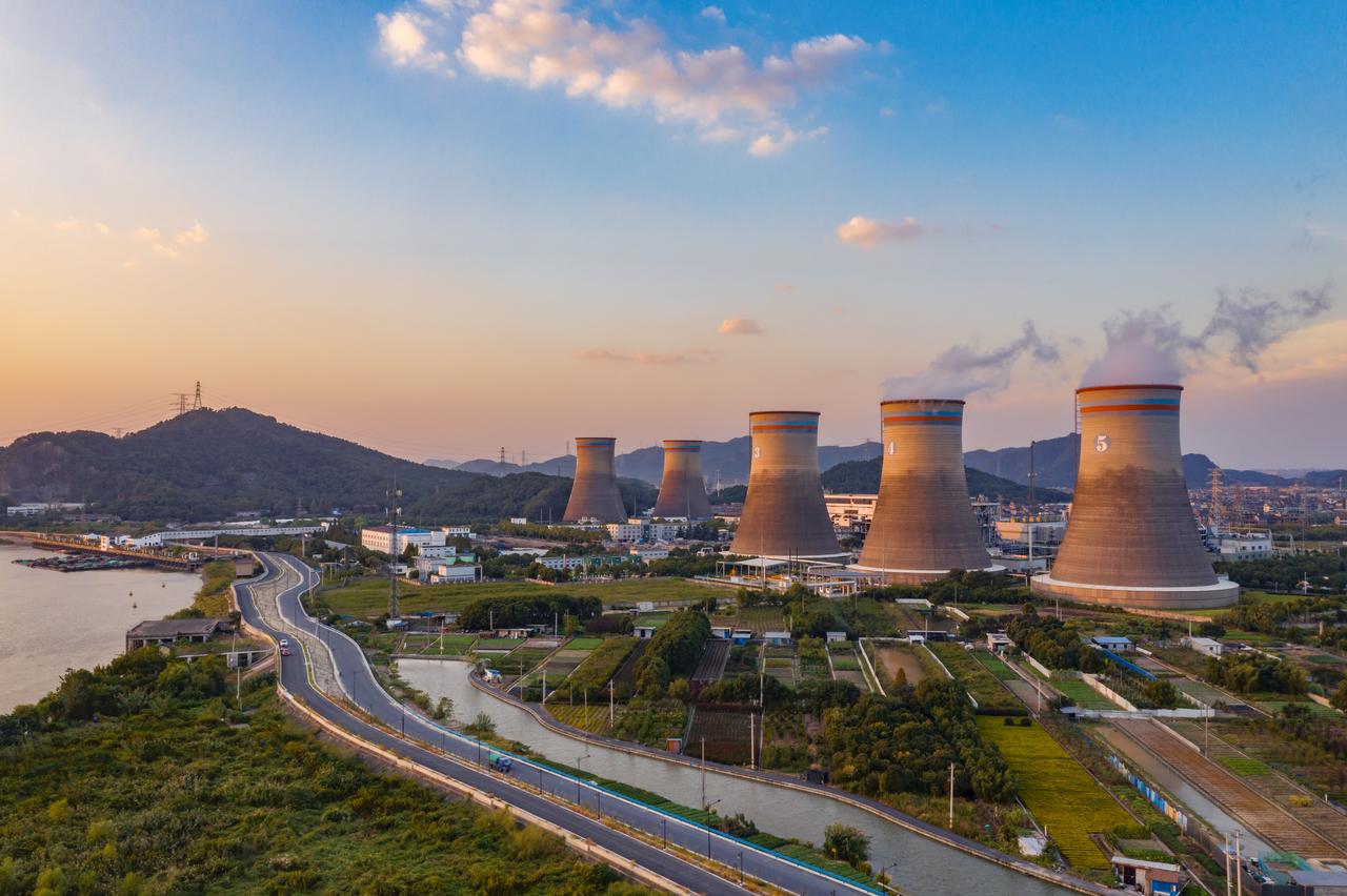 Aerial view of large power plant featuring cooling towers along riverbank. (Photo via Adobe Stock)