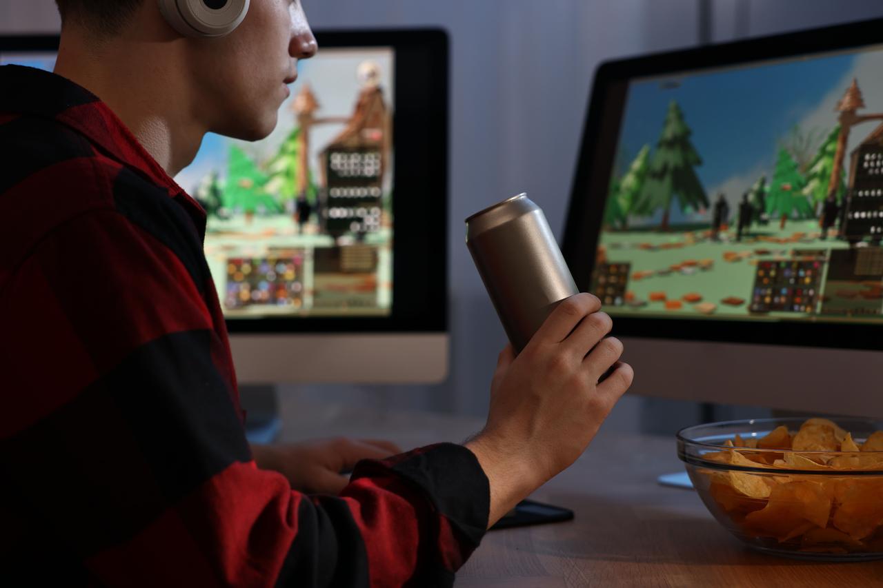 A gamer plays a video game while drinking an energy drinks (Adobe Stock Photo)