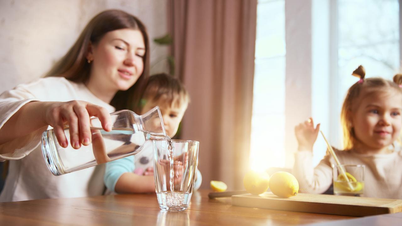 A woman pours water for children at home. (Adobe Stock Photo)