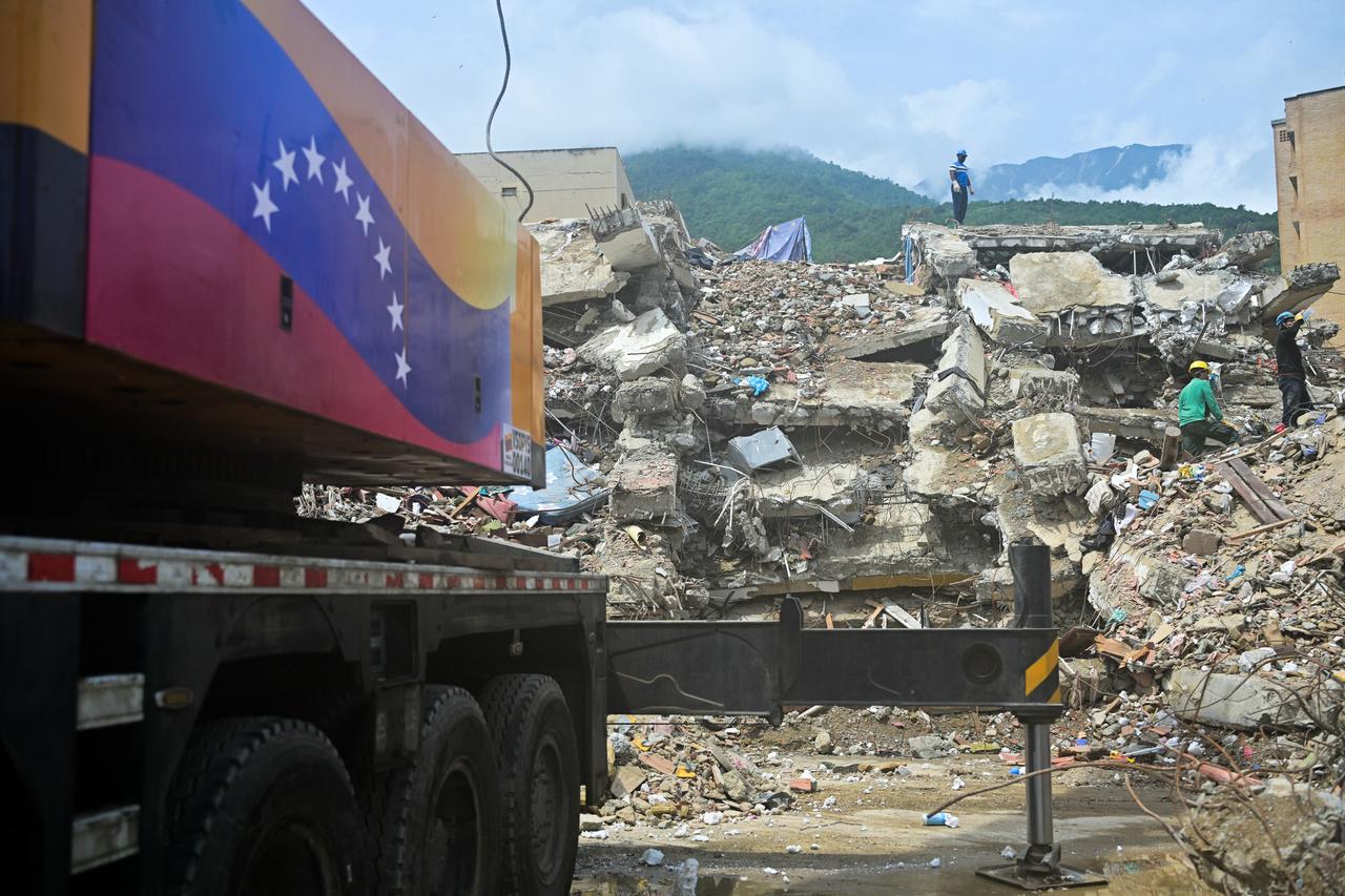Workers remove debris beside a mobile crane bearing the Venezuelan flag at the site of a collapsed building in Caraballeda, La Guaira state, Venezuela, on July 12, 2026, following twin earthquakes that struck the region. (AFP Photo)