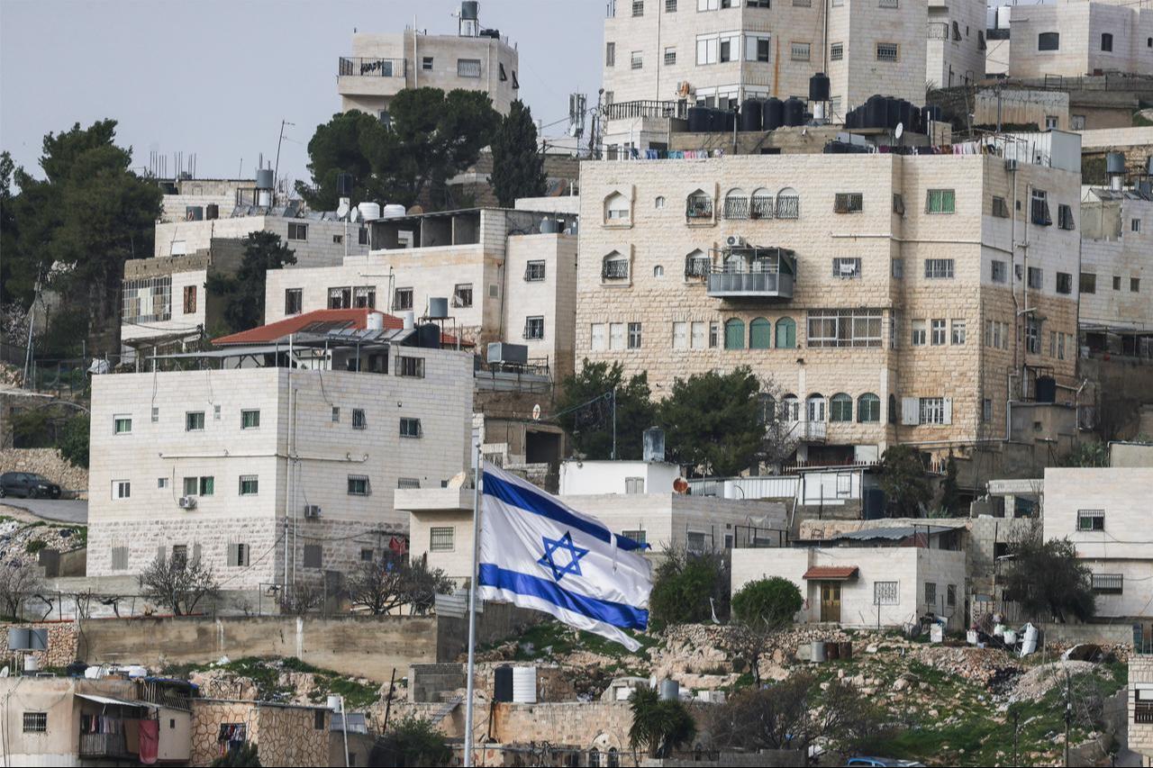 An Israeli flag fluttering above the Israeli settlement of Beit Romano (unseen), with Palestinian buildings in background, in Israeli-occupied West Bank city of Hebron, February 9, 2026. (AFP Photo)