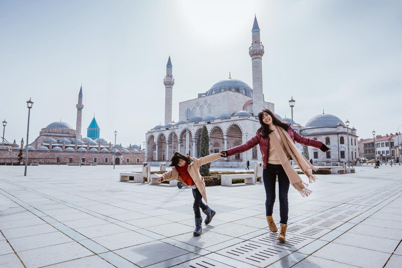 Mother playing around with her daughter in the square while visiting mosque in konya türkiye. (Photo via Adobe Stock)