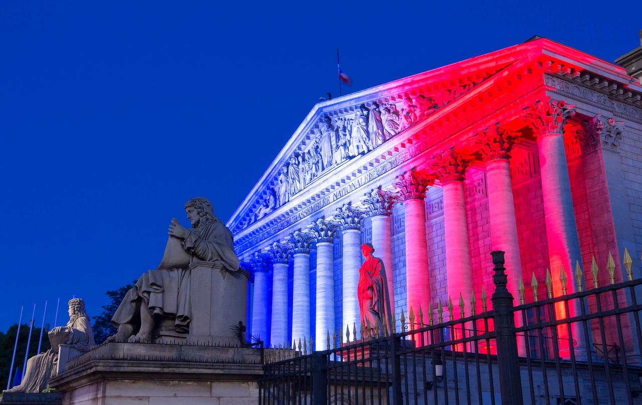The French National Assembly's facade lit up with colors of French national flag at night, Paris, France. (Photo via Adobe Stock)
