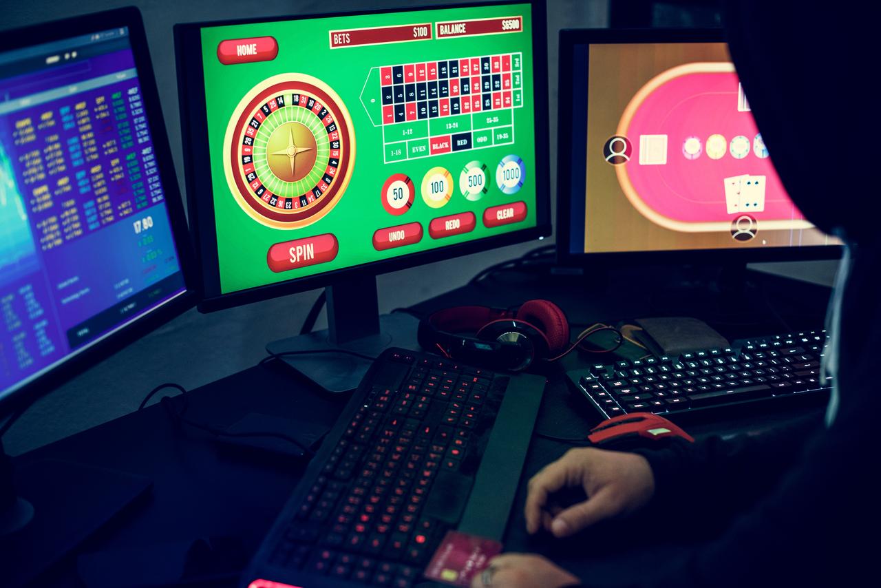 A person uses multiple computer screens to access online gambling and betting platforms. (Adobe Stock Photo)