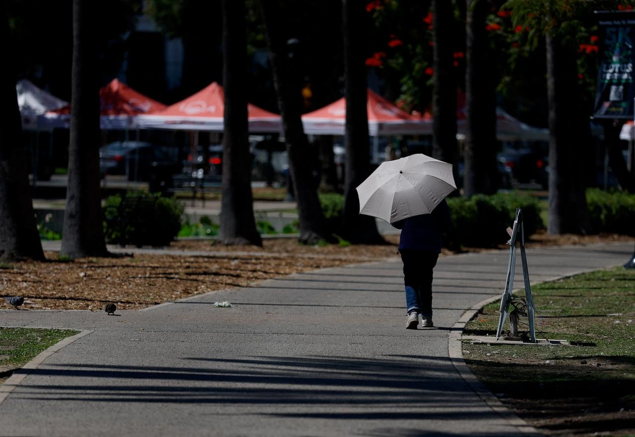 A pedestrian uses an umbrella to shield herself from the sun while walking at Echo Park in Los Angeles, California, July 08, 2026. (AFP Photo)